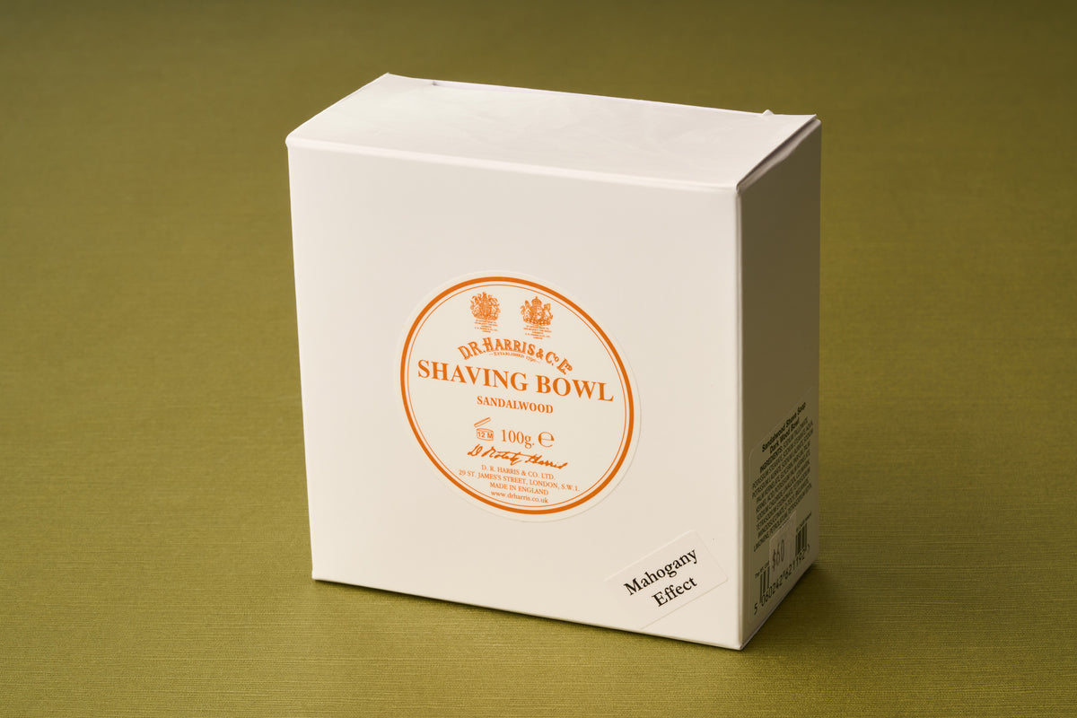 A white box labeled “D.R. Harris Sandalwood Shaving Soap” with orange text and a small note reading “Mahogany Effect,” set on an olive green surface—ideal for those seeking a premium shaving soap for a zero-waste routine.