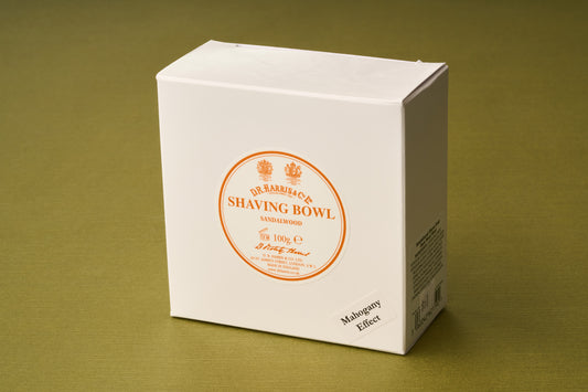 A white box labeled “D.R. Harris Sandalwood Shaving Soap” with orange text and a small note reading “Mahogany Effect,” set on an olive green surface—ideal for those seeking a premium shaving soap for a zero-waste routine.