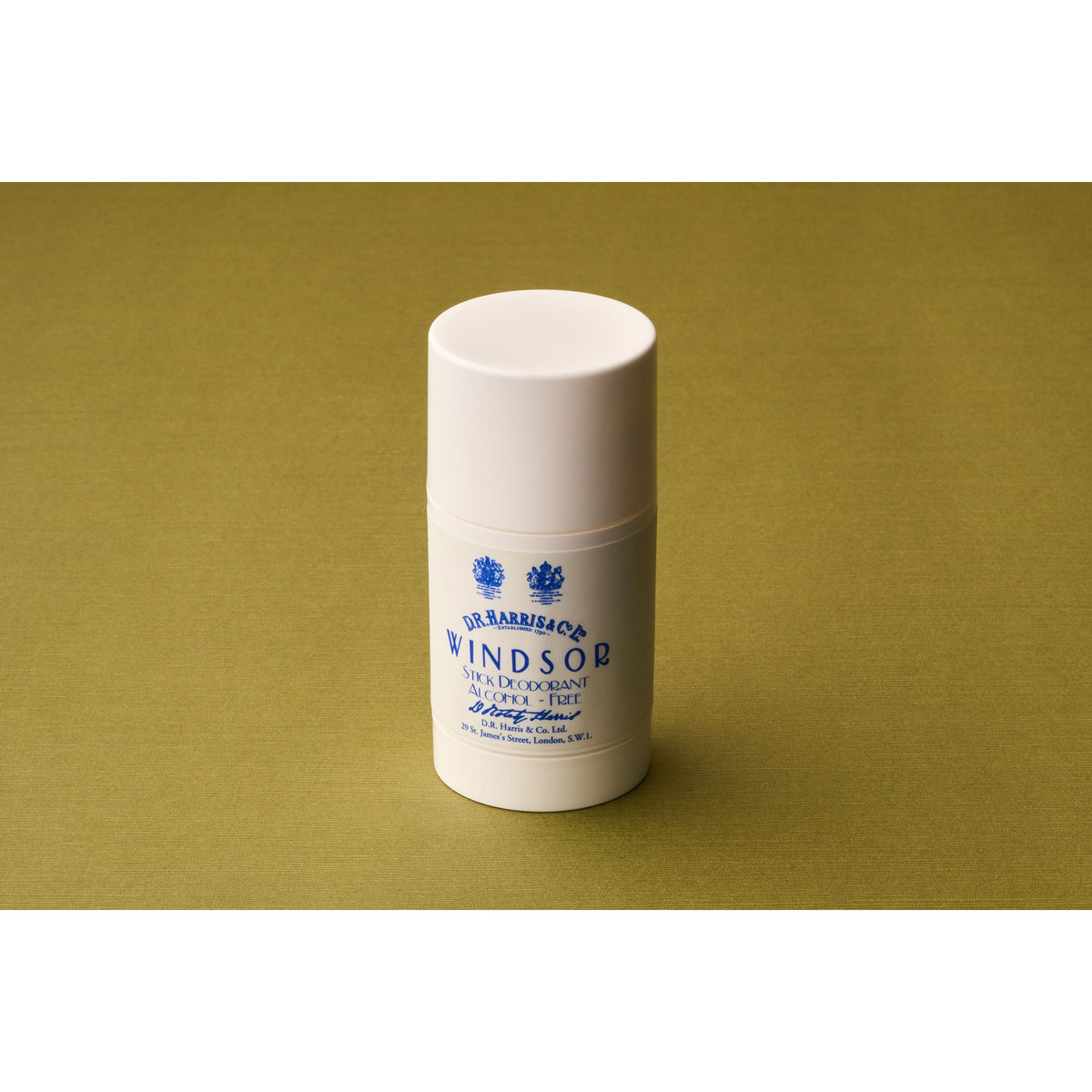A white cylindrical stick labeled “D.R. Harris Windsor Deodorant Stick” stands upright on a plain olive-green surface, providing an alcohol-free deodorant experience with the signature Windsor scent.