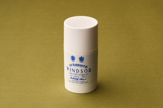 A white cylindrical stick labeled “D.R. Harris Windsor Deodorant Stick” stands upright on a plain olive-green surface, providing an alcohol-free deodorant experience with the signature Windsor scent.