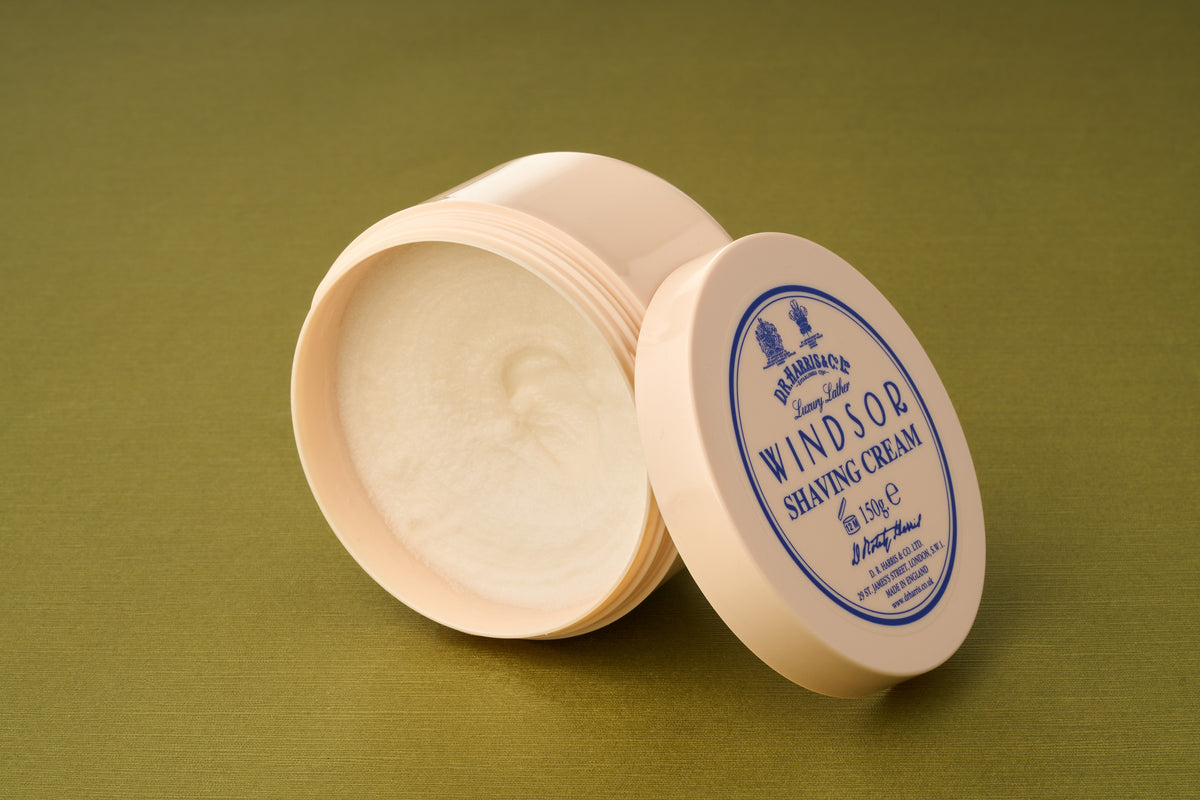 An open container of D.R. Harris Windsor Shaving Cream, with its lid set to the side, is displayed on a green surface.