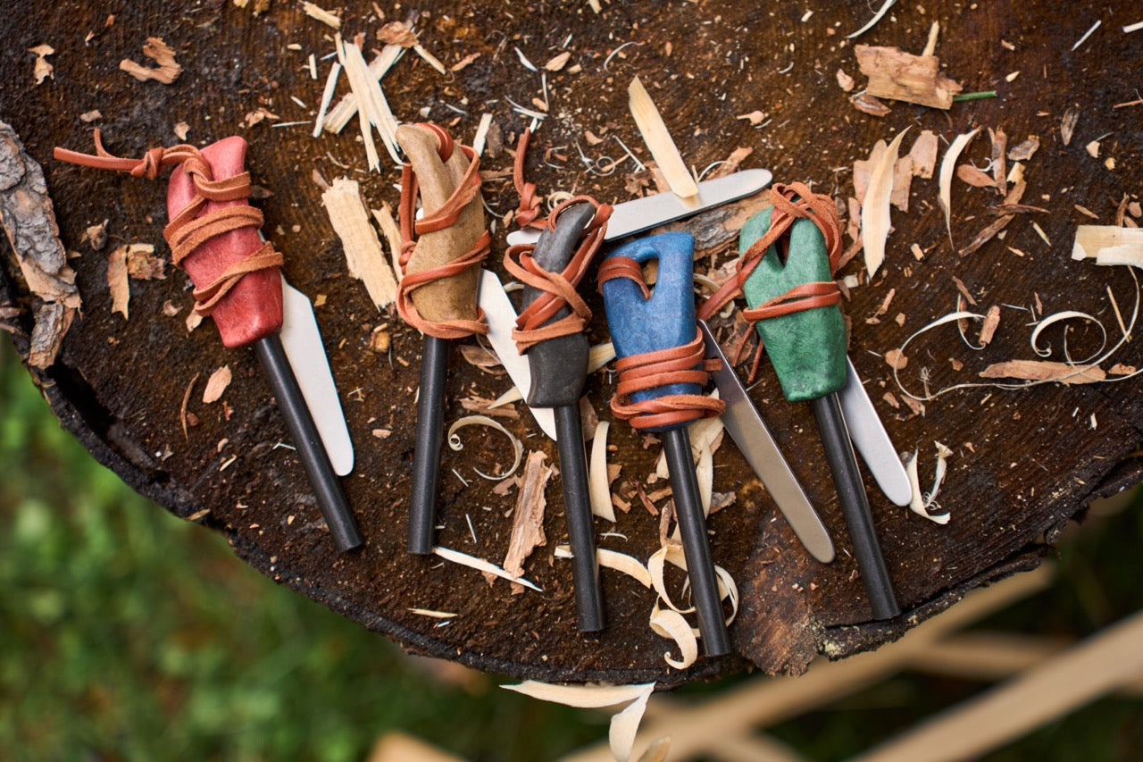 Set of small fire steels with leather wraps on a wooden surface with wood shavings.