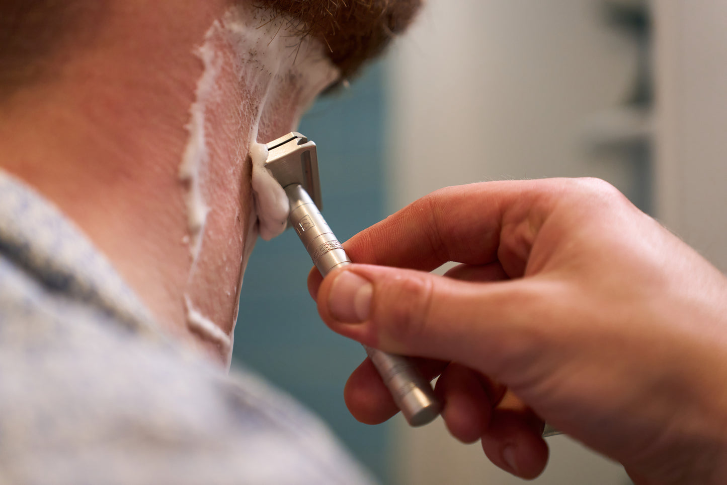 A person shaves the back of their neck using the Henson Safety Razor Aircraft Aluminum and shaving cream for a smooth finish. Only their hand, the razor, and part of their neck are visible.