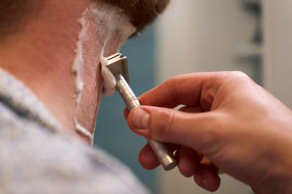 A person shaves the back of their neck using the Henson Safety Razor Aircraft Aluminum and shaving cream for a smooth finish. Only their hand, the razor, and part of their neck are visible.