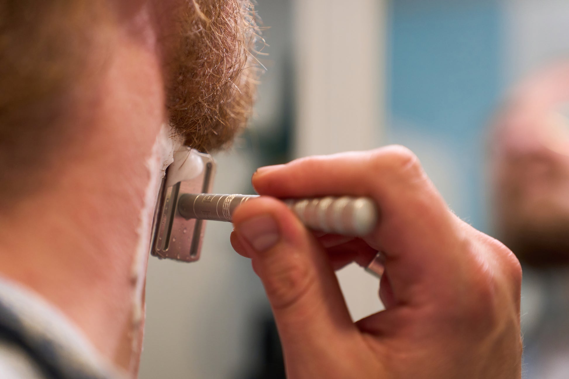 A close-up of a person shaving their neck with the Henson Safety Razor Aircraft Aluminum, carefully applying shaving cream to their skin.