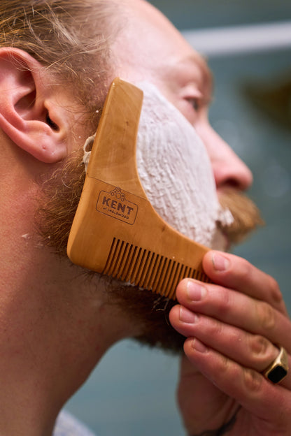A person uses the Kent of Inglewood Beard Shaper as a beard trimming tool to shape their beard while shaving, with shaving cream applied to their cheek.