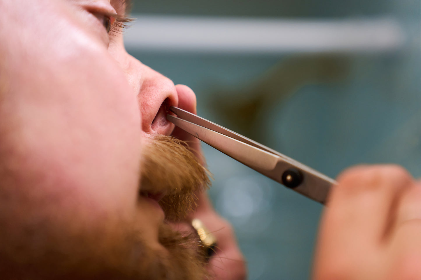 A close-up of a person using Rockwell Hair and Beard Scissors for precision trimming of their nose hair, with focus on the nose and mustache area.