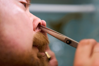 A close-up of a person using Rockwell Hair and Beard Scissors for precision trimming of their nose hair, with focus on the nose and mustache area.