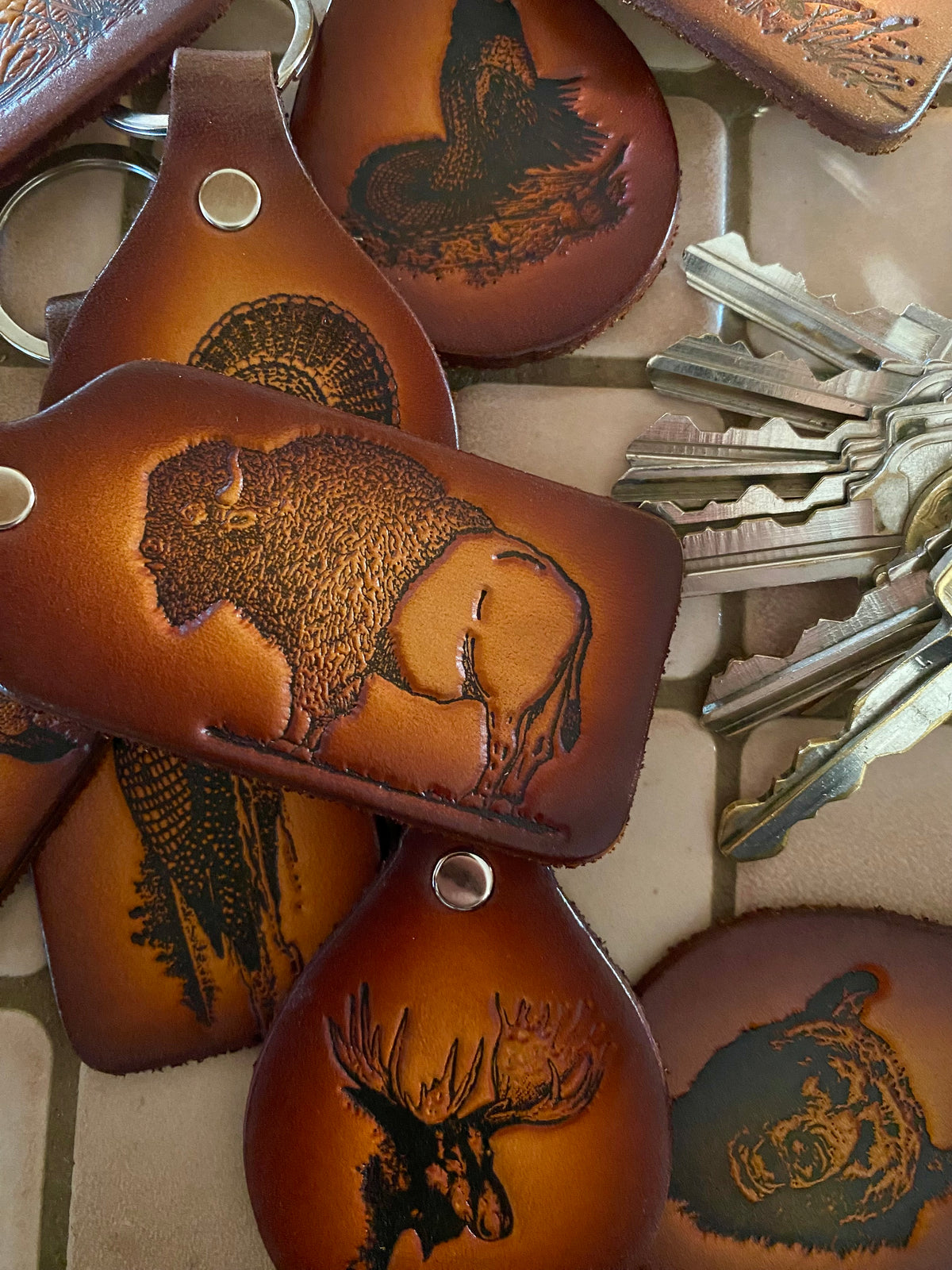 Handmade Leather Wildlife Keychain featuring embossed buffalo, moose, and bear designs resting next to a set of metal keys.