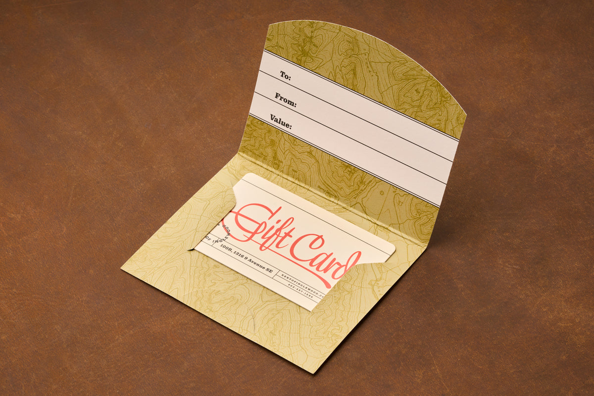 An open Gift Card holder from Kent of Inglewood displays spaces labeled To, From, and Value. Inside is a card marked “Gift Card,” ideal for barber services or distinctive shaving gifts. The holder sits on a brown surface.