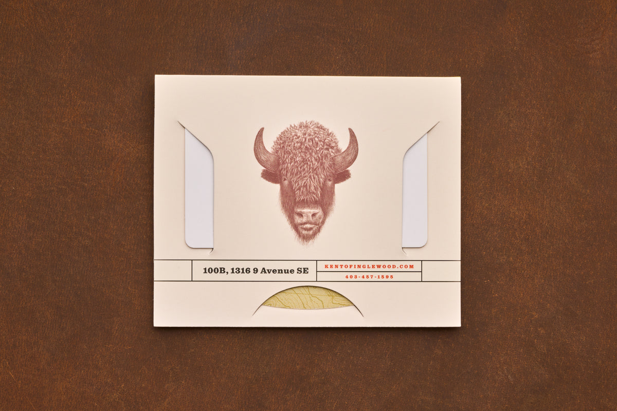 A cream envelope featuring a buffalo illustration, business address, and contact details rests on a brown surface. The envelope displays two flaps and a partial gold seal at the bottom—an ideal presentation for the Shaving Class Gift Card or other grooming essentials like straight razor shaving tips.