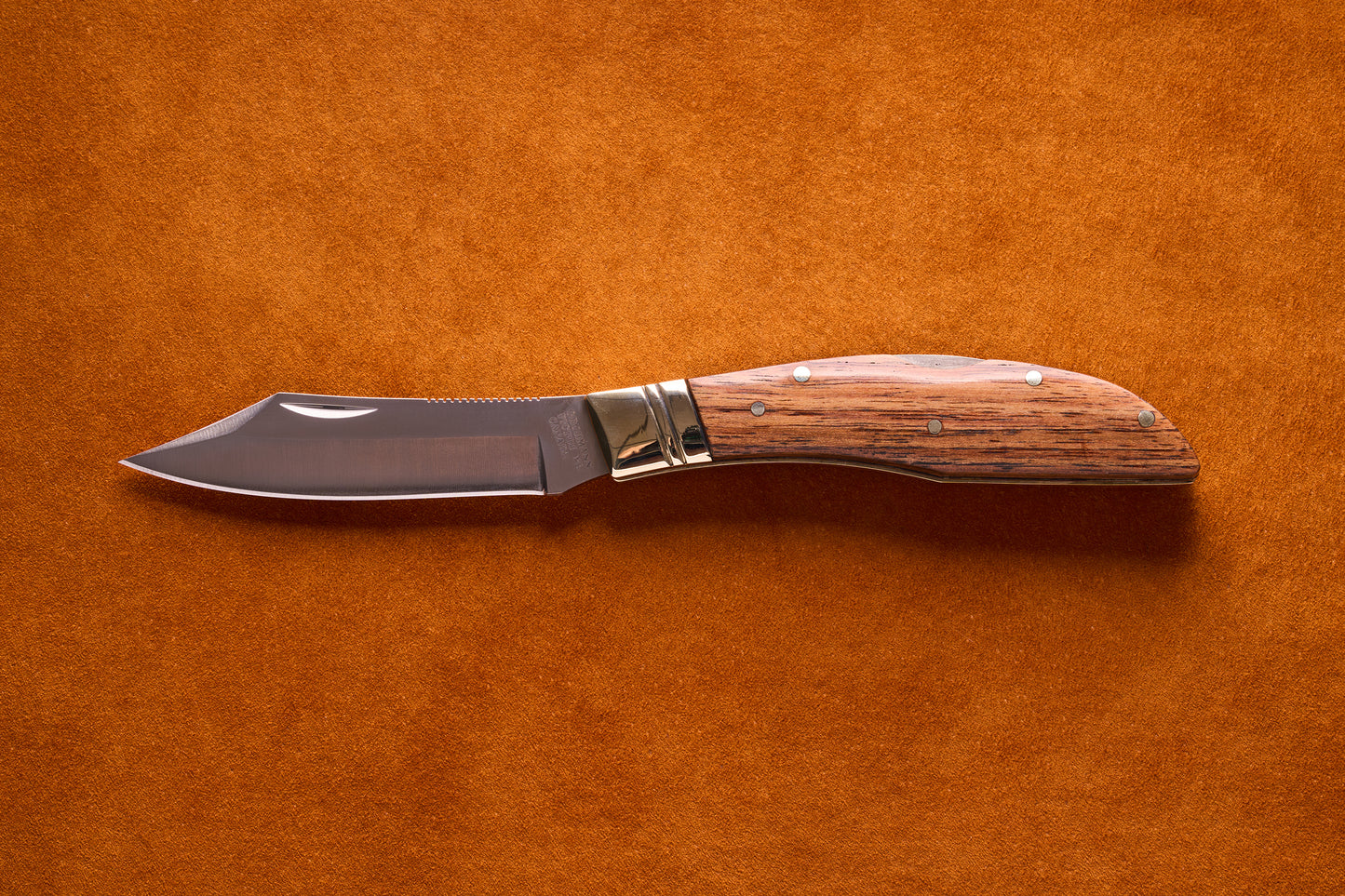 Grohmann Mini Russell Lockblade with Rosewood Handle, 4 Clip Point, featuring a polished steel blade on a suede surface, showcasing its compact design and craftsmanship.