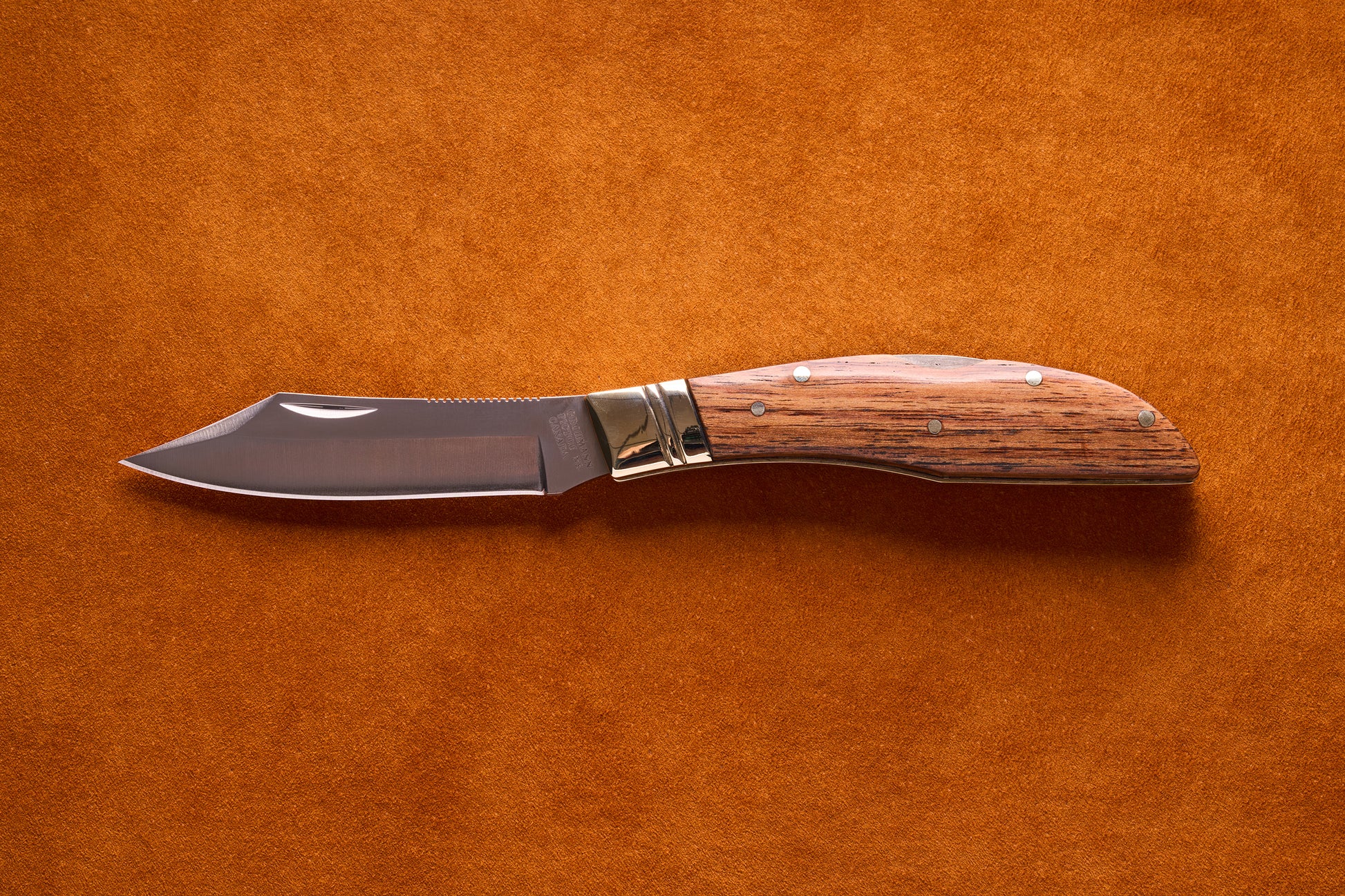 Grohmann Mini Russell Lockblade with Rosewood Handle, 4 Clip Point, featuring a polished steel blade on a suede surface, showcasing its compact design and craftsmanship.