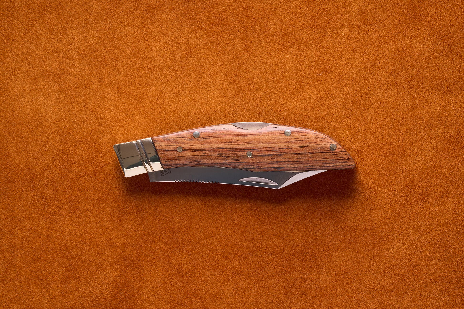 Grohmann Mini Russell Lockblade with Rosewood Handle, 4 Clip Point, featuring a stainless steel blade, rests on an orange background, showcasing its compact, versatile design.