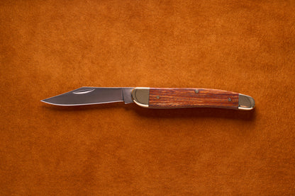 Grohmann Pocket Knife with Silver and Rosewood Handle, 4, featuring a stainless steel blade and brass bolsters, laid open on a textured background.