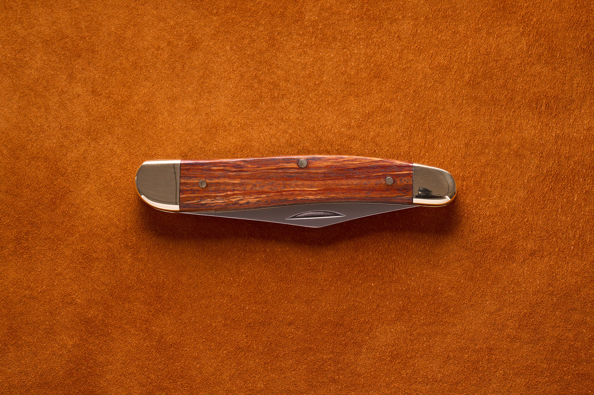 Grohmann Pocket Knife with Silver and Rosewood Handle, 4, on leather surface, showcasing its polished metal bolsters and stained wood grain.
