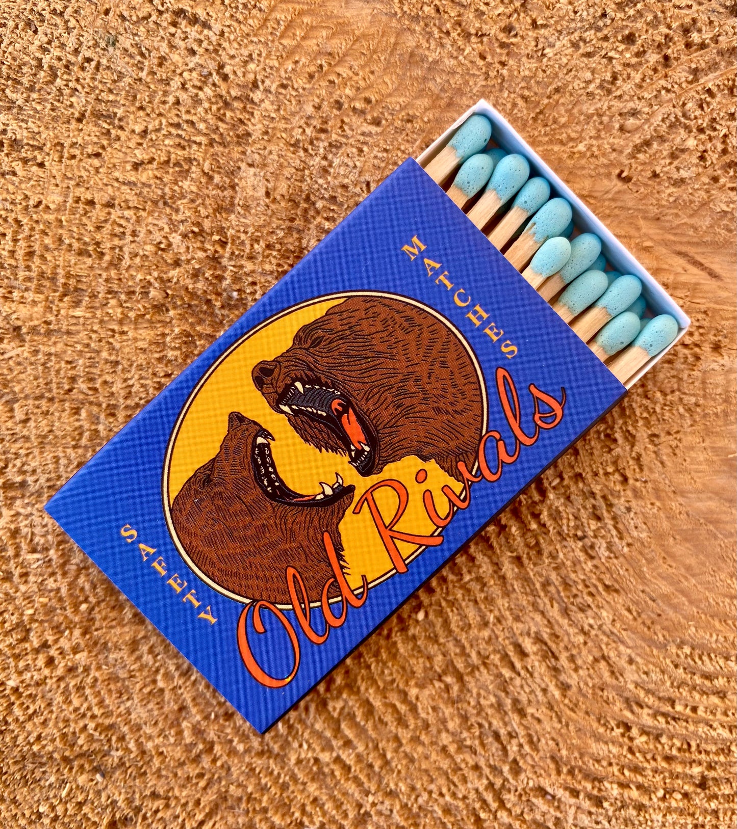 Matchbox with bear illustration and 'Old Rivals' text on a wooden surface