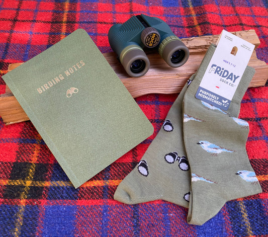 Green notebook, binoculars, and bird-themed socks on a plaid fabric background