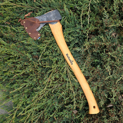 The Hultafors Ekelund Small Felling Axe, featuring a Swedish carbon steel blade and American hickory handle, rests on dense green foliage with its leather sheath covering the edge.