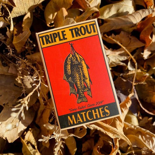 Triple Trout matches packaging surrounded by dried leaves
