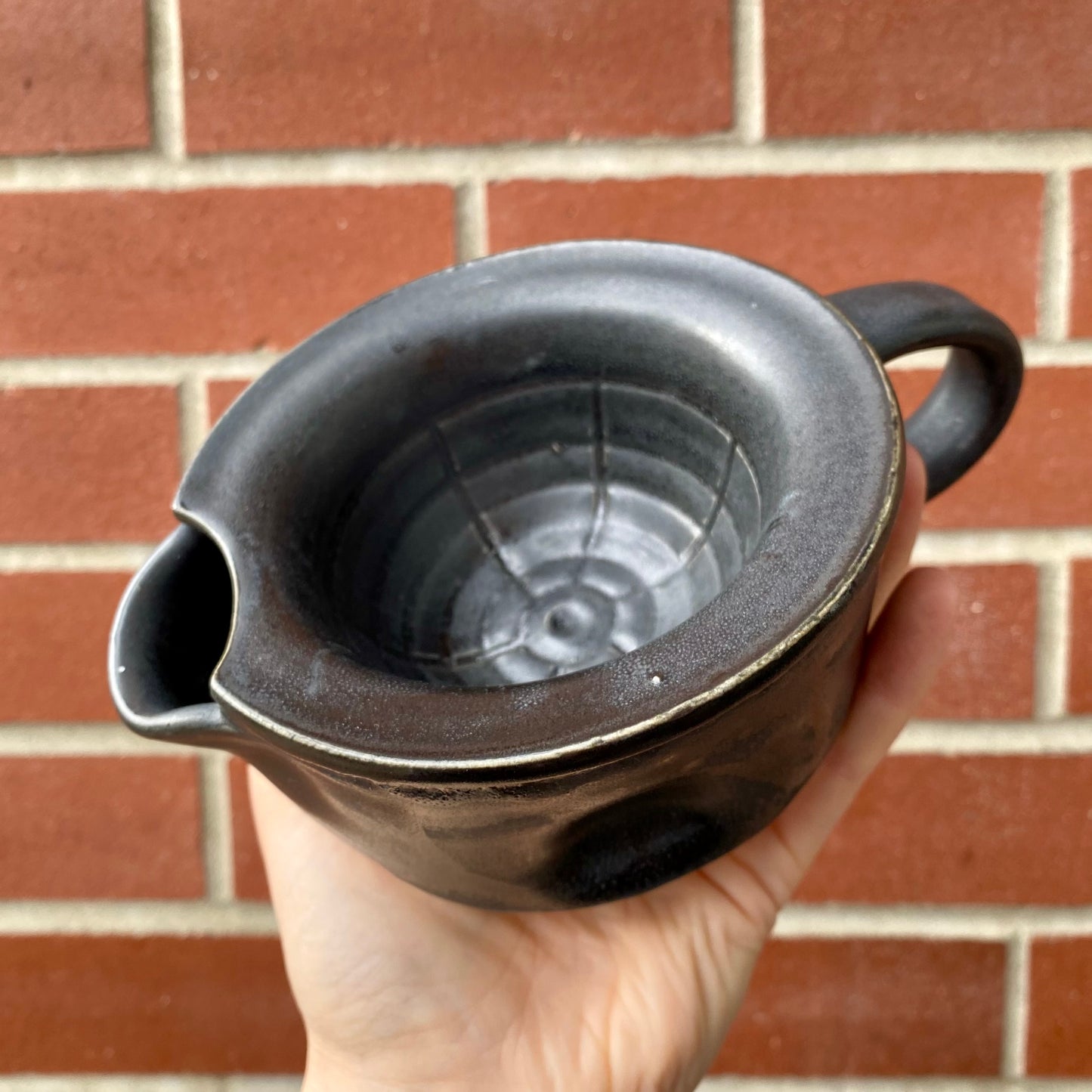 Hand holding a black ceramic filter against a brick wall background