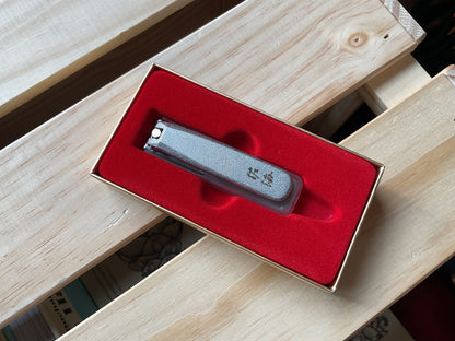 A Touroku Sakai Nail Clipper with Japanese characters etched on the metal handle, resting in a red velvet-lined presentation box.