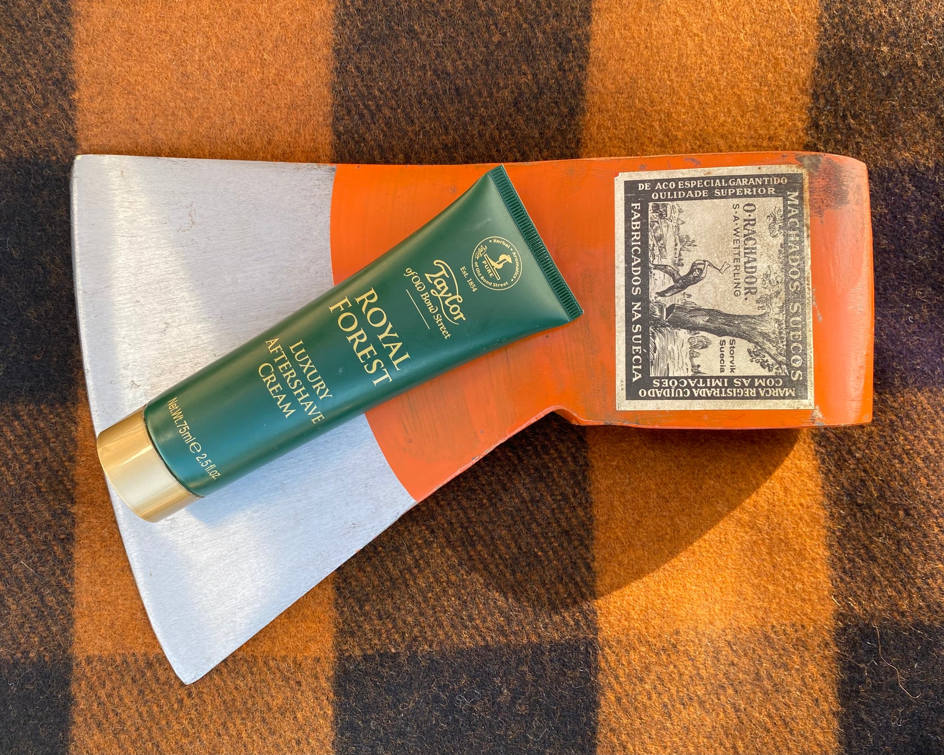Taylor of Old Bond Street Royal Forest Aftershave Cream on an orange axe head, enhances post-shave care, providing soothing hydration and irritation relief.