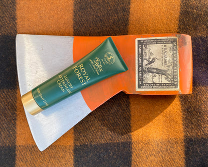 Taylor of Old Bond Street Royal Forest Aftershave Cream on an orange axe head, enhances post-shave care, providing soothing hydration and irritation relief.