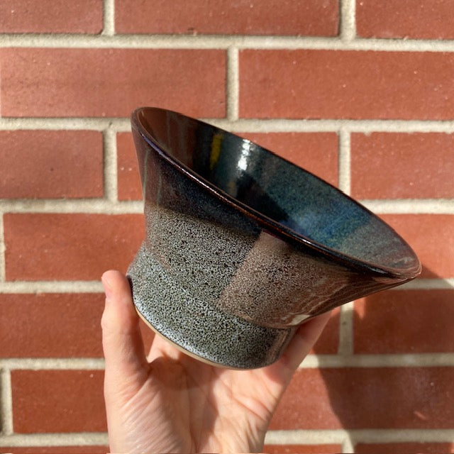 A hand holds a Sosan Fong Shave Bowl, showcasing its speckled gray-blue glaze, flared rim, and narrow base, ideal for lathering shaving cream.