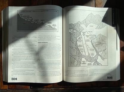 Open textbook from Survival Wisdom & Know-How, showcasing glacier cross-sections on pages 504-505, illustrating mountaineering challenges and techniques, laid on a wooden surface.