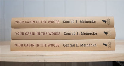 Stack of three Your Cabin in the Woods hardcover books by Conrad E. Meinecke, ideal for nature and homebuilding enthusiasts, on a light-wood shelf.