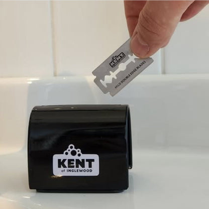 Hand dropping a double-edge razor blade into a Kent of Inglewood Razor Blade Bank on a sink, illustrating safe and responsible blade disposal.