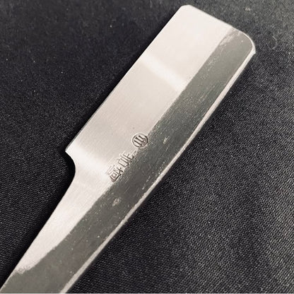 Iwasaki Kamisori close-up, showcasing its precision-crafted straight-razor blade with stamped characters and logo, highlighting quality craftsmanship and ergonomic design for superior shaving.