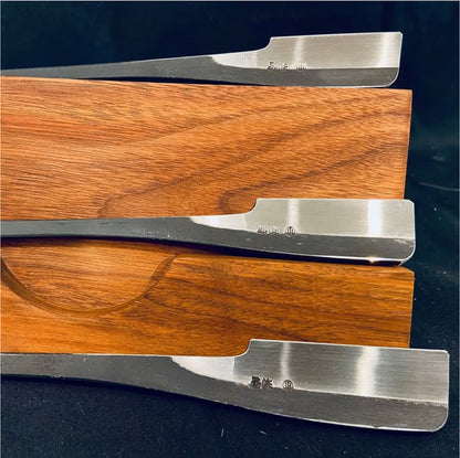 Iwasaki Kamisori: Three polished steel chisel blades on a wooden block, showcasing beveled cutting edges and square tangs for handle attachment.