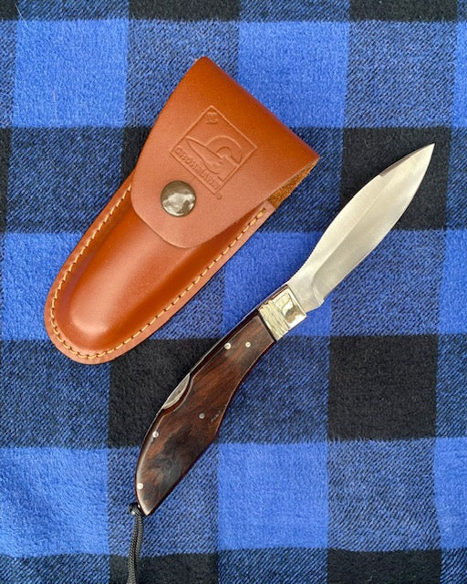 Knife with wooden handle and leather sheath on a blue checkered fabric background