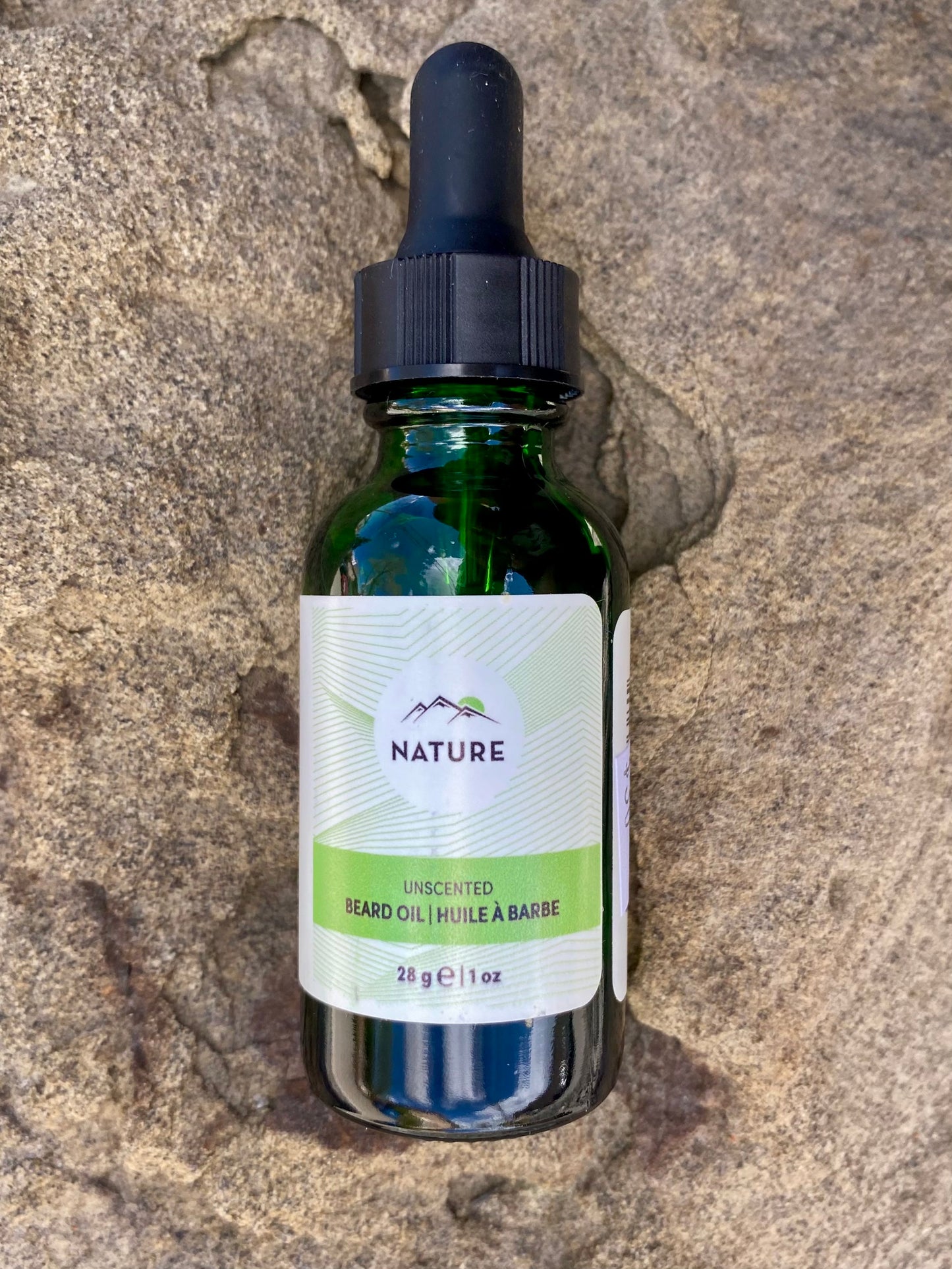 A green glass dropper bottle labeled Banff Beard Co. Nature Beard Oil, 28g/1oz, rests on a textured stone, highlighting a premium unscented and moisturizing grooming oil for those seeking natural beard care.