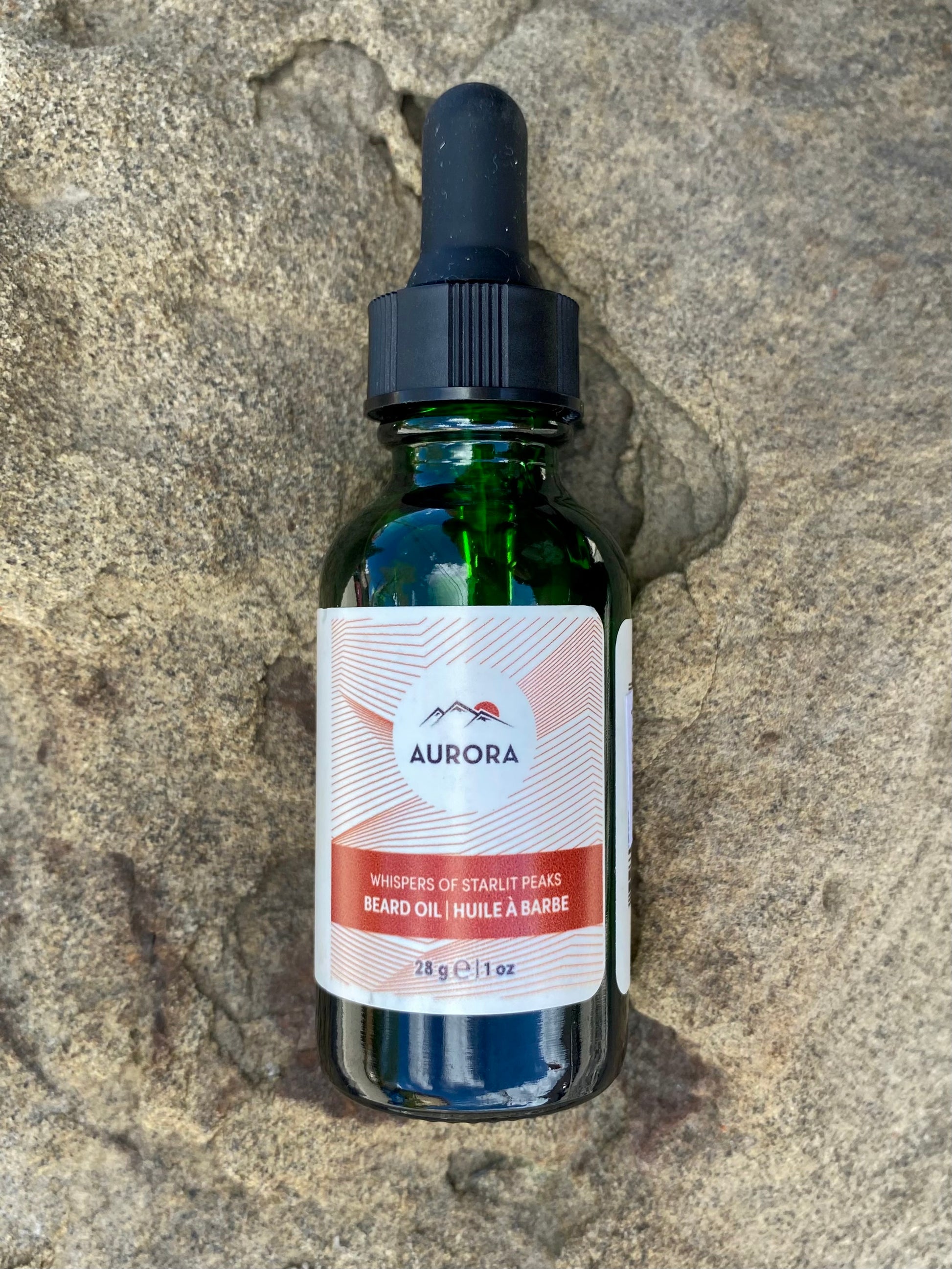 A green glass dropper bottle labeled Banff Beard Co. Aurora Beard Oil, with a black cap, rests on textured stone. The 28g (1oz) bottle contains premium ingredients to elevate your grooming routine.