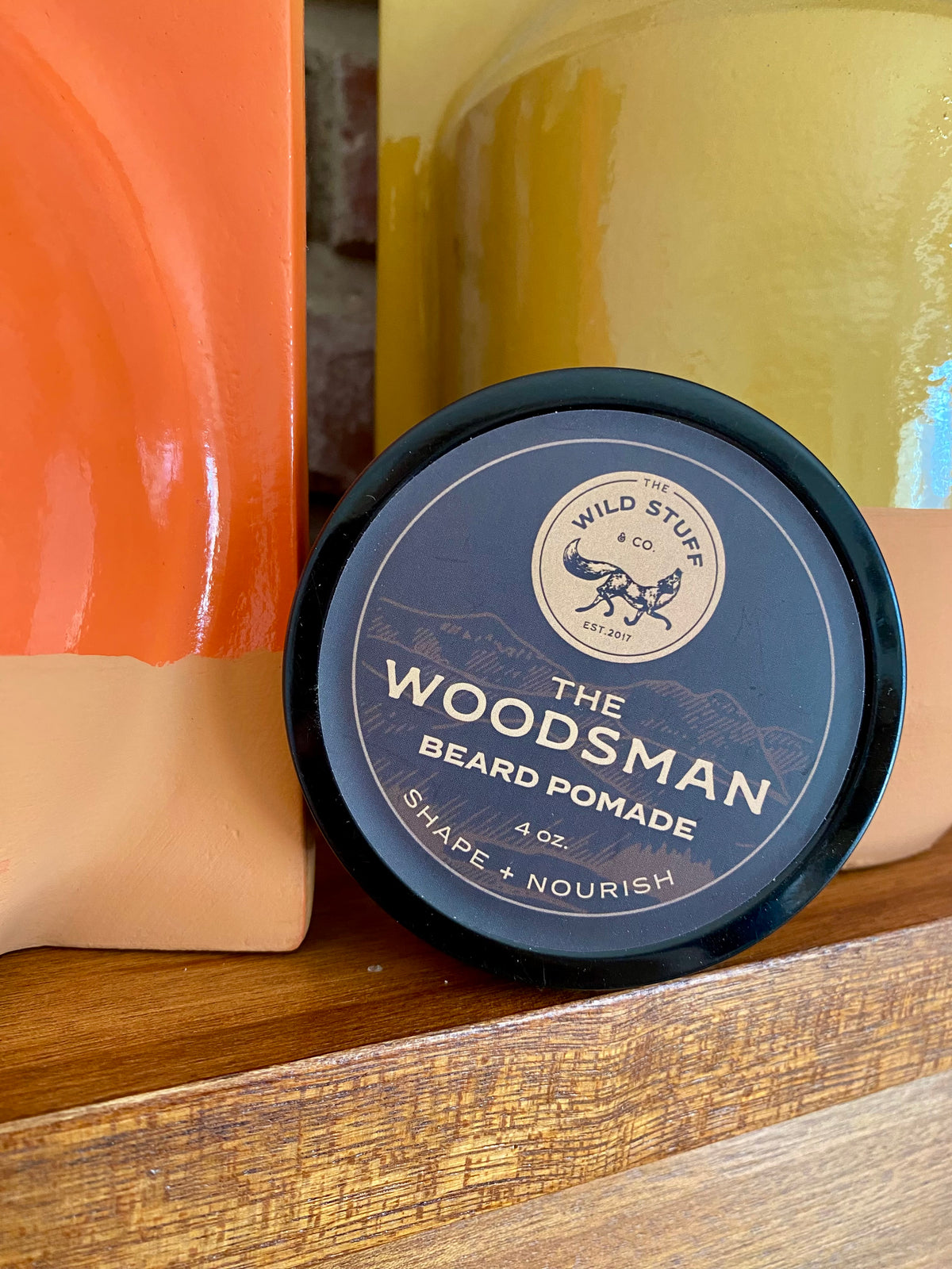 A circular tin of Wild Stuff & Co. Woodsman Beard Pomade with a black lid featuring a fox logo and the text The Woodsman Beard Pomade.