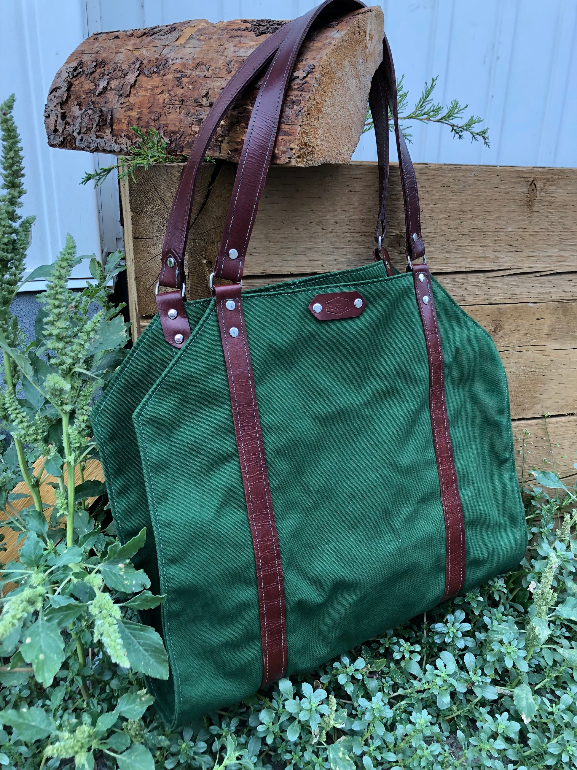 Horace & Jasper Log Carrier with leather straps, ideal for transporting logs cleanly and stylishly, showcased against a rustic wooden backdrop with greenery.