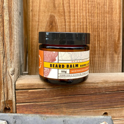 Kent of Inglewood Spice Beard Balm in an amber jar, offering light hold and moisture for facial hair grooming, on a rustic wooden shelf.