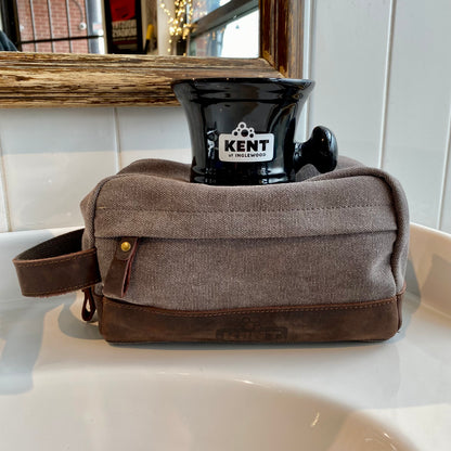 Dopp Kit & Shaving Mug Bundle on a sink, featuring a grey canvas dopp kit with brown leather trim and a branded Kent of Inglewood black ceramic shaving mug.