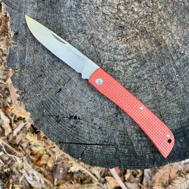 Maserin Scout 163 folding pocket-knife with stainless steel blade and textured red handle, resting open on a tree-stump, showcasing its sleek, modern design.