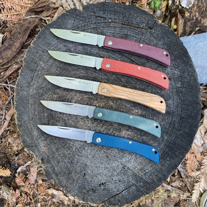 Maserin Scout 163 folding pocket knives displayed on a tree stump, showcasing sleek D2 steel blades and Micarta or Olive wood handles.
