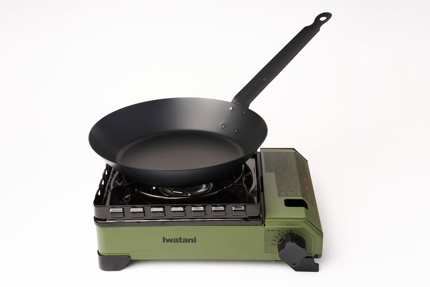 A black frying pan sits on top of a green Iwatani Cassette Konro "Tough Maru" Portable Stove, set against a plain white background.