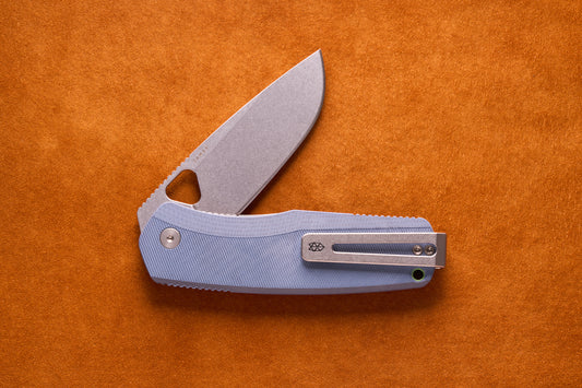 James Folsom Pro folding pocket knife with a stone-washed blade and textured blue handle, featuring upgraded titanium hardware and ambidextrous pocket clip, on a suede surface.