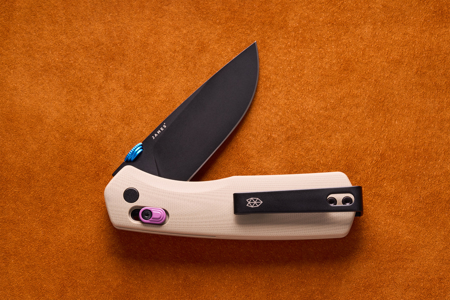 James Carter folding pocket knife with black drop-point blade, light G10 handle, blue thumb-stud, purple lock-slider, and black pocket clip, on orange suede.