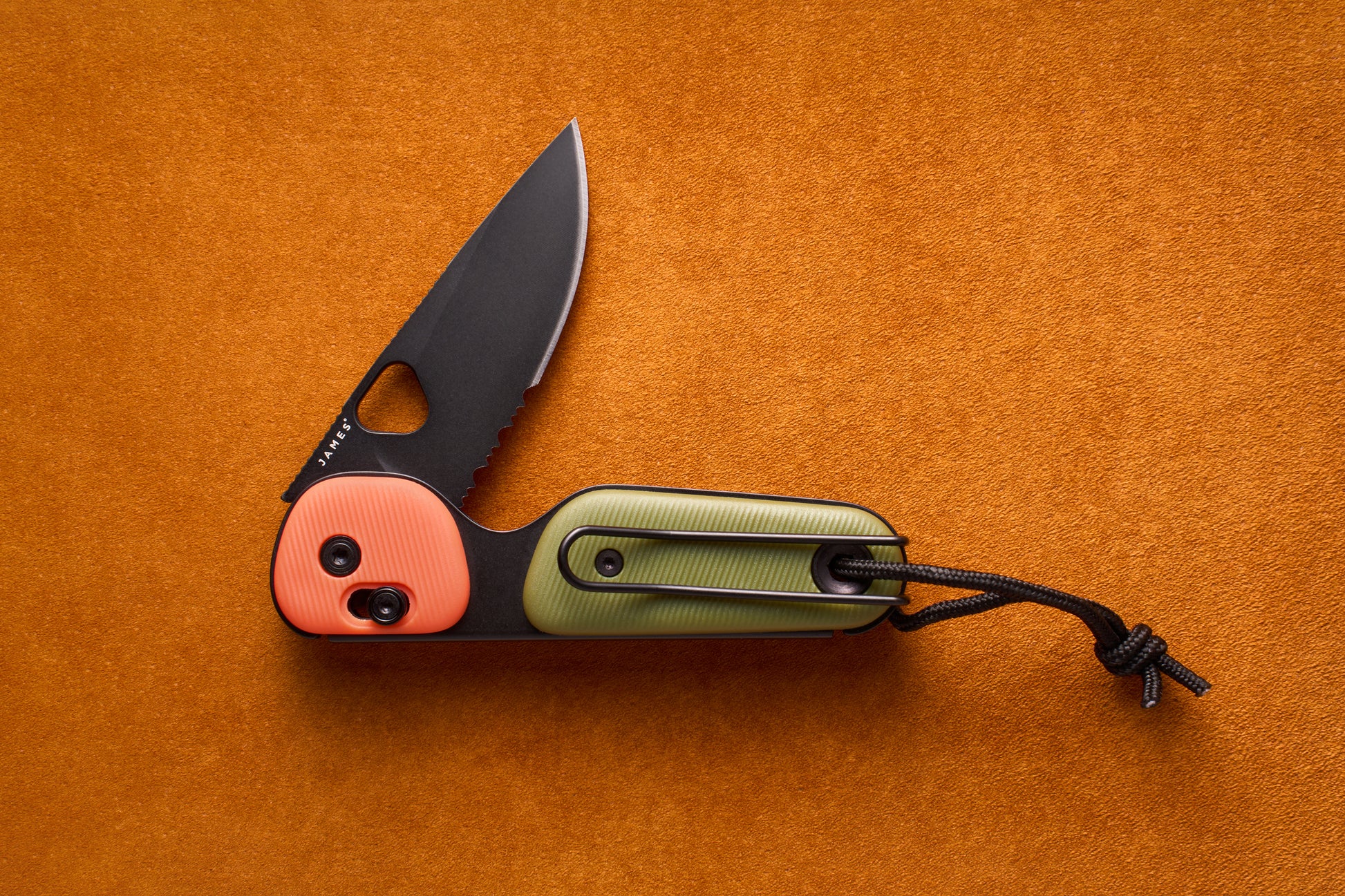 The James Redstone—a folding pocket knife featuring a partially serrated black blade, an orange and green handle, and a black lanyard, designed for everyday carry—is displayed on an orange textured surface.