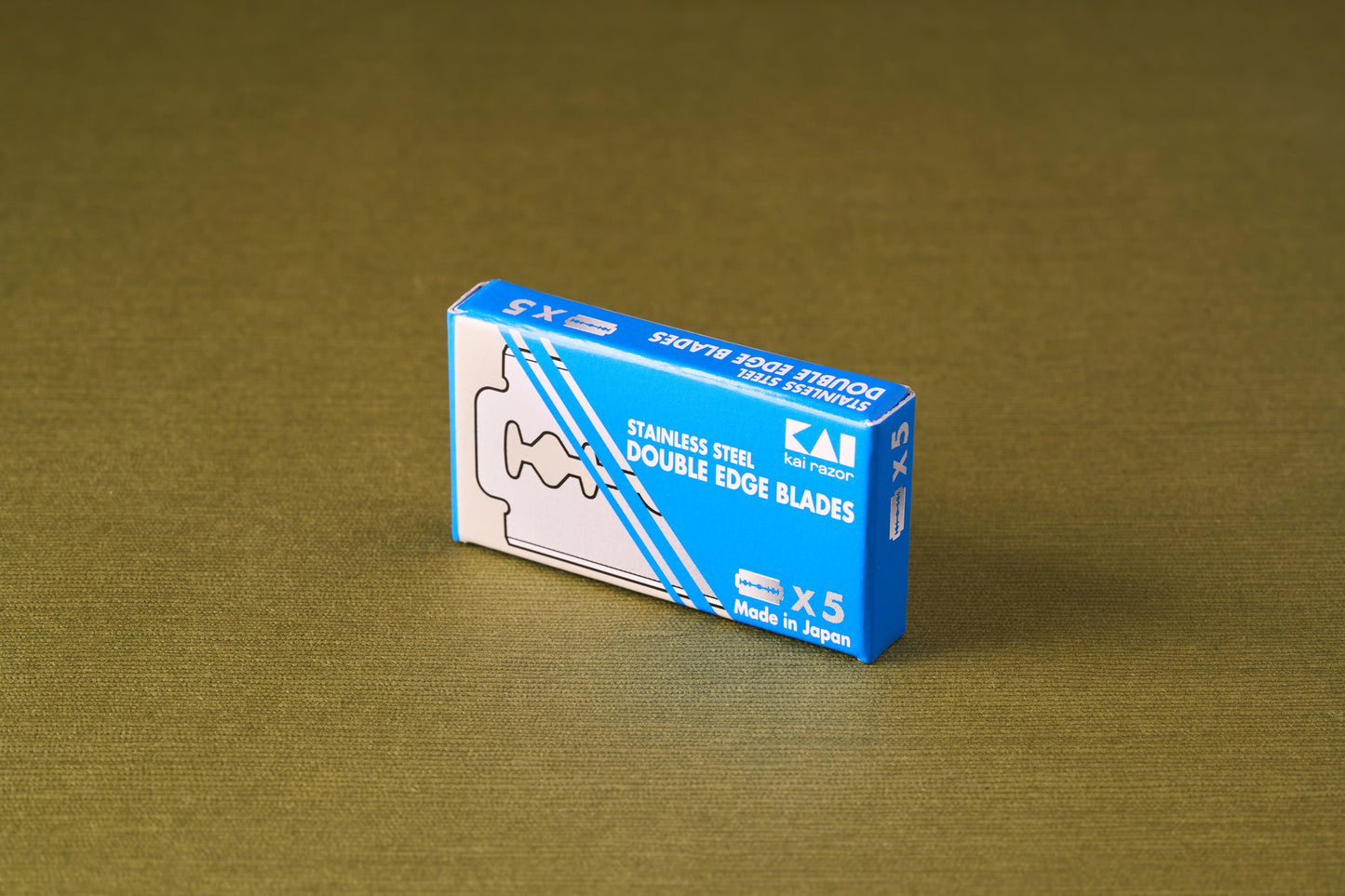 Kai Double Edge Razor Blades, 5 Pack, in a blue box on fabric, offering precision shaving with Japanese craftsmanship.