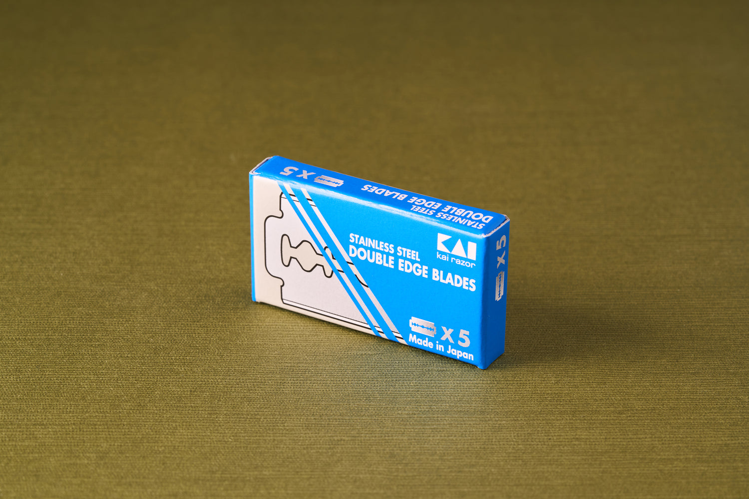Kai Double Edge Razor Blades, 5 Pack, in a blue box on fabric, offering precision shaving with Japanese craftsmanship.