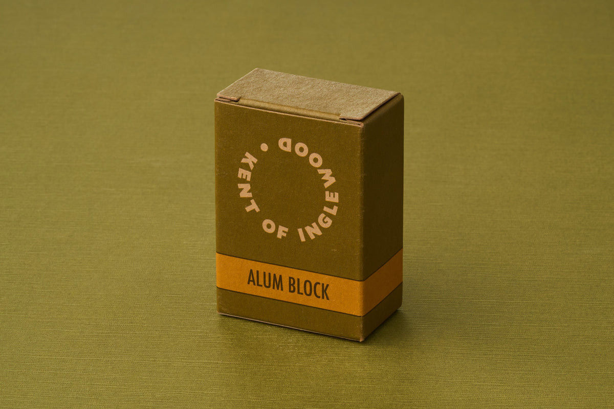 A compact, olive-green box labeled “Kent of Inglewood Potassium Alum Block” stands upright on a coordinating green surface, evoking the classic grooming benefits of potassium alum—a natural mineral often favored as a deodorant.